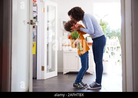 Amare il figlio dando madre mazzo di fiori per celebrare la festa della mamma a casa Foto Stock