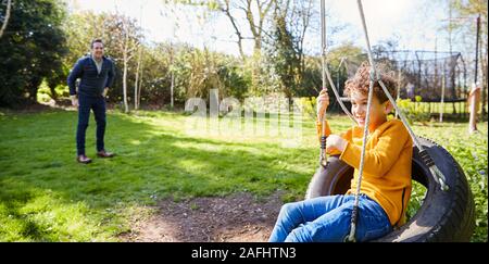 Padre e Figlio Divertirsi sul pneumatico oscillante nel giardino di casa Foto Stock