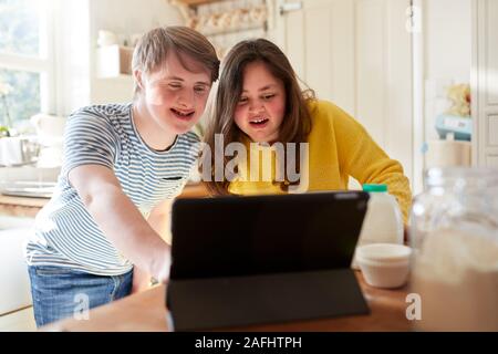 Giovani sindrome Downs giovane ricetta seguente sulla tavoletta digitale per cuocere la torta nella cucina di casa Foto Stock