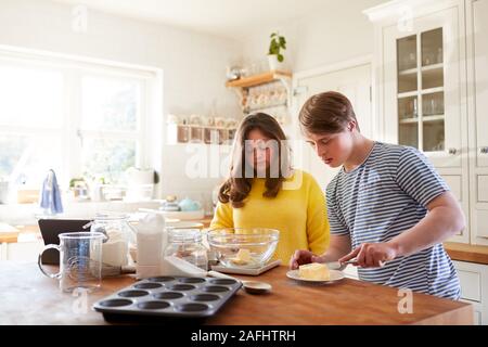 Giovani sindrome Downs giovane ricetta seguente sulla tavoletta digitale per cuocere la torta nella cucina di casa Foto Stock