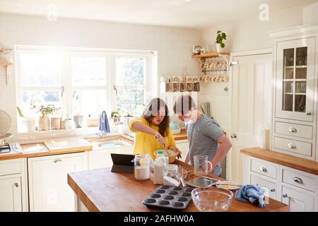 Giovani sindrome Downs giovane ricetta seguente sulla tavoletta digitale per cuocere la torta nella cucina di casa Foto Stock