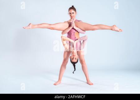 Due ragazze flessibile ginnasti con pig-tail, in rosa leotards sta eseguendo i gruppi usando il supporto durante la posa isolati su sfondo bianco. Close-up. Foto Stock