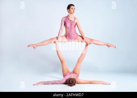 Due ragazze flessibile ginnasti con pig-tail, in rosa leotards sta eseguendo i gruppi usando il supporto durante la posa isolati su sfondo bianco. Close-up. Foto Stock