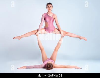 Due ragazze flessibile ginnasti con pig-tail, in rosa leotards sta eseguendo i gruppi usando il supporto durante la posa isolati su sfondo bianco. Close-up. Foto Stock