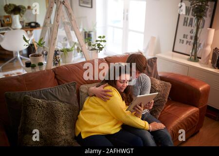 Giovani sindrome Downs giovane seduto sul divano con tavoletta digitale in casa Foto Stock