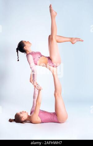 Due ragazze flessibile ginnasti in rosa leotards sono facendo esercizi usando il supporto e posa isolati su sfondo bianco. Close-up. Foto Stock