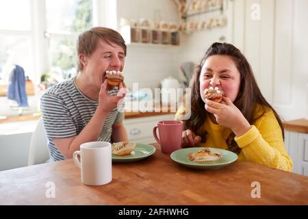 Giovani sindrome Downs giovane godendo di tè e una fetta di torta in cucina a casa Foto Stock
