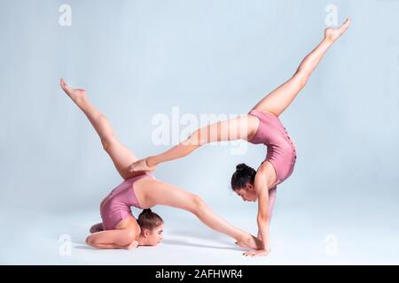 Due ragazze flessibile ginnasti in rosa leotards sono facendo esercizi usando il supporto e posa isolati su sfondo bianco. Close-up. Foto Stock