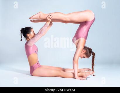 Due ragazze flessibile ginnasti in rosa leotards sono facendo esercizi usando il supporto e posa isolati su sfondo bianco. Close-up. Foto Stock