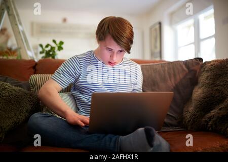 Giovani la sindrome di Down uomo seduto sul divano utilizzando portatile a casa Foto Stock