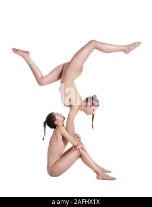 Due ragazze flessibile ginnasti in beige leotards sta eseguendo esercizi capovolta usando il supporto e posa isolati su sfondo bianco. Close-up. Foto Stock