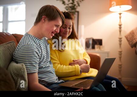 Giovani sindrome Downs giovane seduto sul divano utilizzando portatile a casa Foto Stock