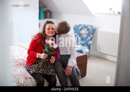 Amare i giovani la sindrome di Downs giovane seduto sul letto con Uomo Donna dando fiori Foto Stock