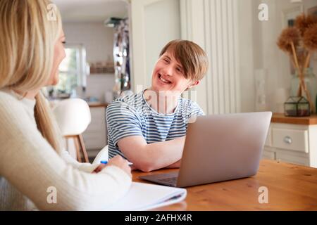 La sindrome di Down Uomo seduto con il Tutor di casa utilizzando computer portatile per la lezione a casa Foto Stock