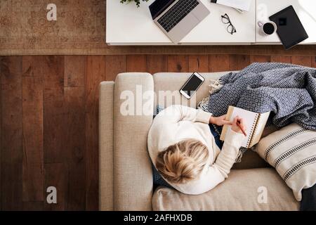 Scatto dall'alto guardando verso il basso sulla donna che lavorano come i Social Media Influencer a casa sdraiato sul divano Foto Stock