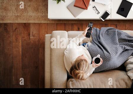 Scatto dall'alto guardando verso il basso sulla donna a casa sdraiato sul divano guardando la televisione Foto Stock