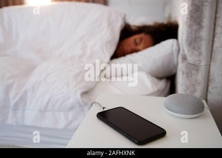 La donna dorme nel letto con telefono mobile e Assistente vocale sul comodino Foto Stock