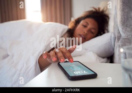 Donna svegliarsi nel letto raggiunge fuori per disattivare la sveglia sul telefono cellulare Foto Stock