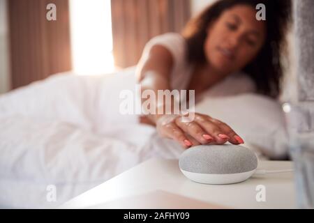 Donna di svegliarvi in letto con Assistente vocale sul comodino accanto a lei Foto Stock