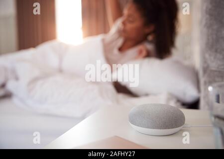 Donna di svegliarvi in letto con Assistente vocale sul comodino accanto a lei Foto Stock