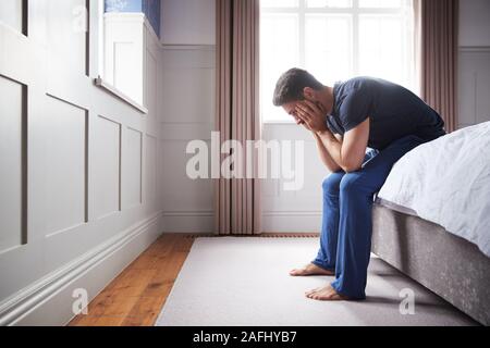 Uomo che indossa pigiama sofferenza con depressione seduta sul letto di casa Foto Stock