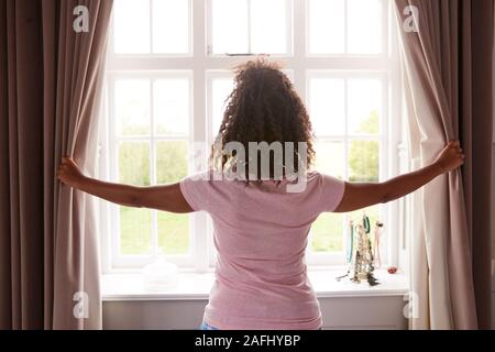 Vista posteriore della donna che indossa pigiama apertura camera da letto tende all inizio di un nuovo giorno Foto Stock