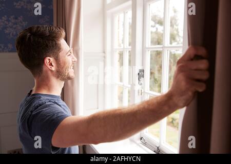 Uomo che indossa pigiama apertura camera da letto tende all inizio di un nuovo giorno Foto Stock