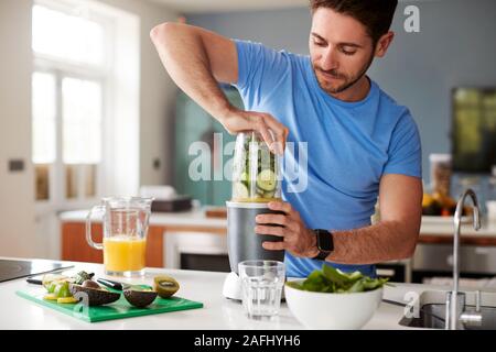 Uomo che fa un succo sano e drink con ingredienti freschi in spremiagrumi elettrico dopo l'esercizio Foto Stock