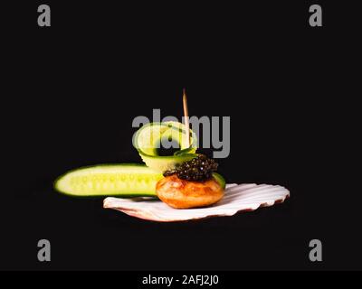 Il caviale nero con il cetriolo, servita su un guscio, close-up su uno sfondo nero con copia spazio. Foto Stock