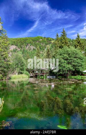 Tranquillo Lago e riflessi di alberi circostanti a Champoluc in Valle d'Aosta, Italia settentrionale sotto una soleggiata cielo blu in un paesaggio panoramico Foto Stock