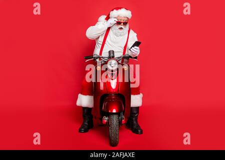 Ritratto di Nizza attraente barbuto scioccato funny funky Santa indossando cap hat seduto sulla bici del motore utilizzando una cella di lettura messaggio sms isolate su Foto Stock