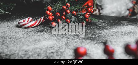 Decorazione di natale con rami di abete e bacche di colore rosso su sfondo scuro. Foto Stock