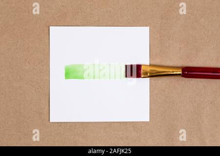Pennello cospargere con della vernice verde a. Cospargere di verde vivace vernice dal pennello su un pezzo di carta bianca Foto Stock