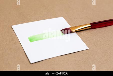 Pennello cospargere con della vernice verde a. Cospargere di verde vivace vernice dal pennello su un pezzo di carta bianca Foto Stock