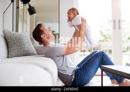 Padre amorevole il sollevamento di 3 mesi bimba in aria nel salotto di casa Foto Stock