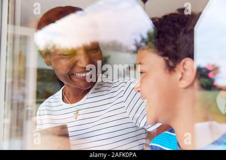 Nonna con il nipote a casa guardando fuori attraverso la finestra sul giardino Foto Stock