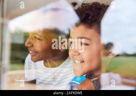 Nonna con il nipote a casa guardando fuori attraverso la finestra sul giardino Foto Stock