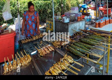 Donna con stallo di grigliata di pesce e calamari su bastoni al mercato del granchio in questa città, famosa per i suoi piatti di pesce; Kep, Cambogia Foto Stock