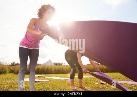 Due femmina matura amici Posa esercizio stuoie su erba a Outdoor ritiro di yoga Foto Stock