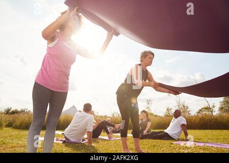 Due femmina matura amici Posa esercizio stuoie su erba a Outdoor ritiro di yoga Foto Stock