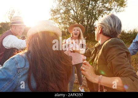 Gruppo di amici maturi rendendo Toast come essi siedono intorno al fuoco e cantare canzoni al campeggio all'aperto Foto Stock