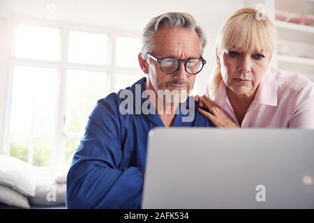 Coppia matura a casa cercando informazioni sulle medicine online utilizzando Laptop Foto Stock