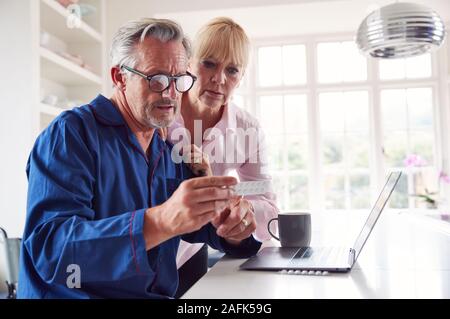 Coppia matura con uomo in sedia a rotelle cercando informazioni sulle medicine online utilizzando Laptop Foto Stock