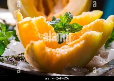 Vista dettagliata del melone fette di melone con la menta e il ghiaccio servita su vintage nastro piatto. Dolce dessert di frutta ancora in vita. Foto Stock