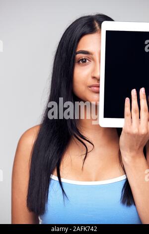 Ritratto in studio di grave giovane donna che ricopre la faccia con tavoletta digitale Foto Stock