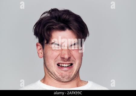 Testa e spalle Studio shot dell'uomo tirando i volti e sorridente in telecamera Foto Stock