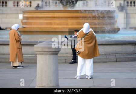 Londra, Inghilterra, Regno Unito. Donna musulmana a fotografare la figlia in Trafalgar Square Foto Stock