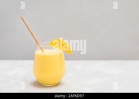 Tradizionale bevanda indiana Mango Lassi in un bicchiere di vetro con carta paglia sul cemento grigio sfondo Foto Stock