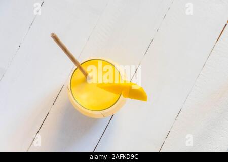 Vista superiore della indian tradizionale bevanda Mango Lassi con carta paglia e mango slice bianco sul tavolo di legno Foto Stock