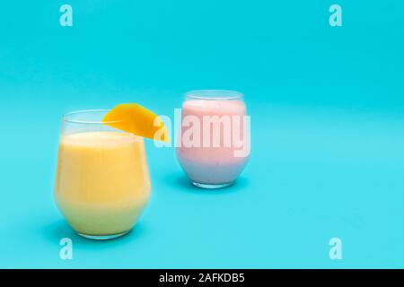 Mango Lassi e fragola Lassi bevande in bicchieri di vetro su sfondo blu Foto Stock
